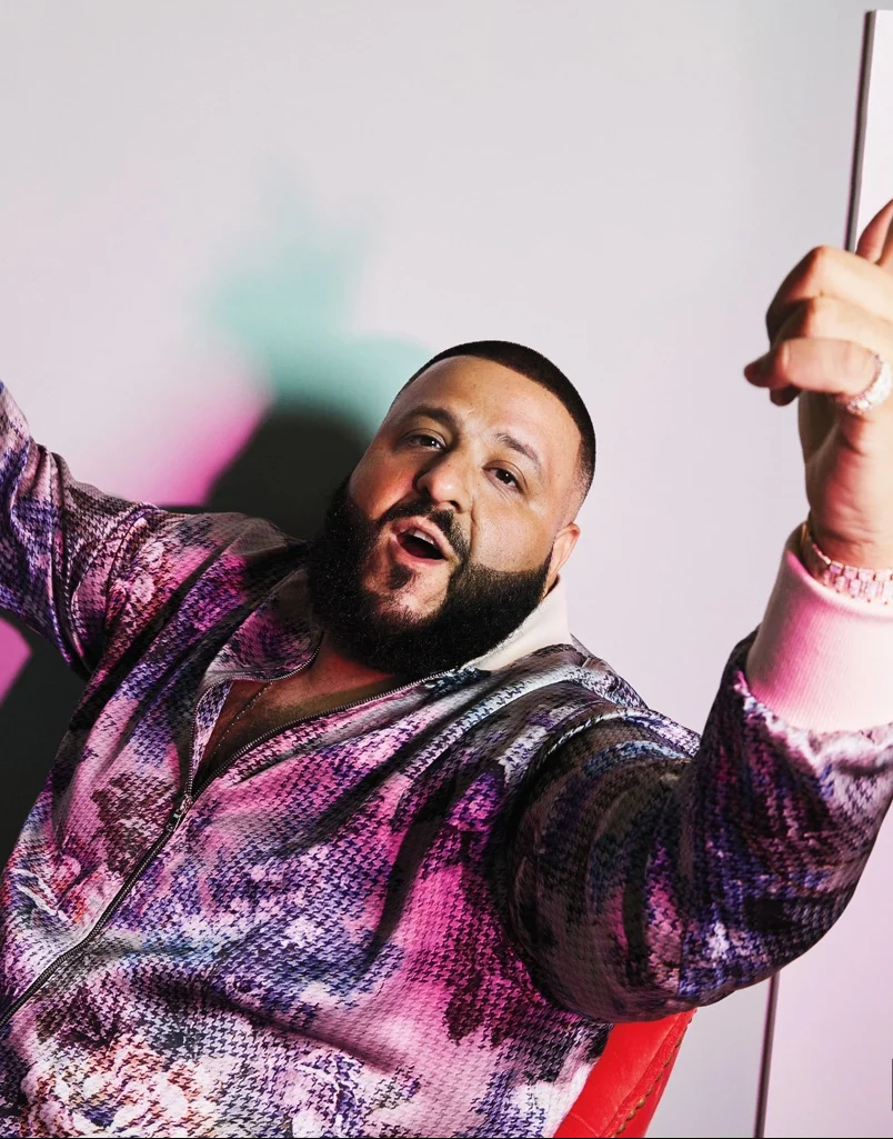 DJ Khaled wearing a purple, white, blue and red digtial print sweater while pointing up with both hands. This image was from the producer's Billboard editorial.