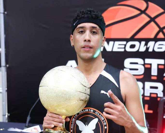 NEON16 Latin artist Kris Floyd posing with his basketball trophy after winning the 2022 All-Star Celebrity Basketball Game powered by Puma, WSS, Vibra Urbana and NEON16. The gam was hosted inMiami and Kris is wearing a black basketball jersey uniform with a visible Puma logo and a butterfly emblam.